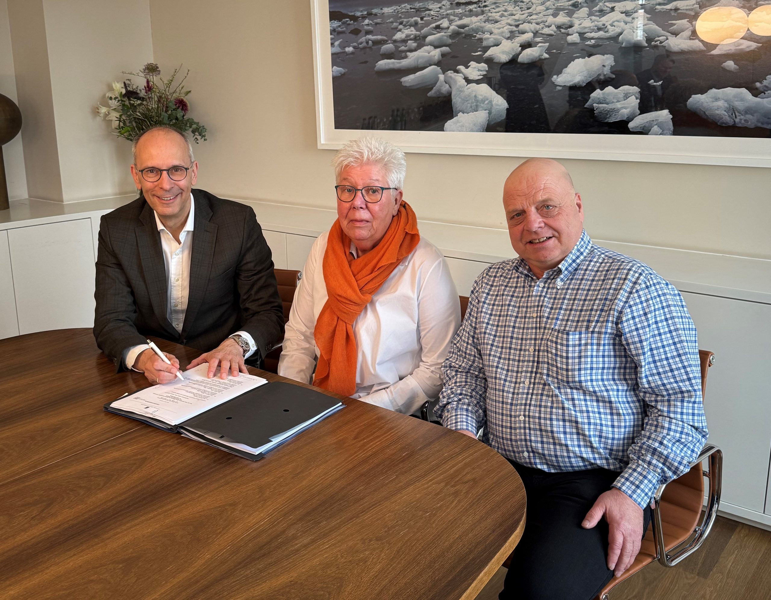 Ein Foto, welches Stefan Falk, Waltraud Tillack und Carsten Hergert abbildet. Alle drei lächeln in die Kamera während Herr Falk seine Unterschrift setzt.