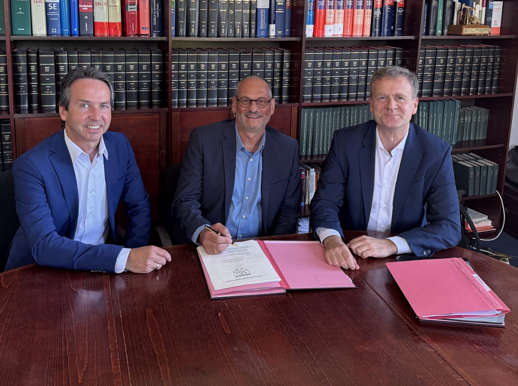 Markus Popp (Omexom), Andreas Glunk (Leukhardt Schaltanlagen GmbH) und Jens Roseneck (Actemium) sitzen lächelnd an einem Tisch während die Unterzeichnung erfolgt.